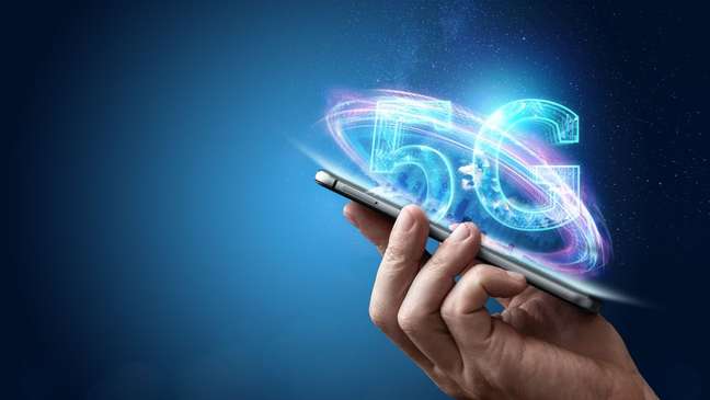 Aparelho celular na mão de uma pessoa e os letreiros 5G saindo da tela como magia, monstrando uma tecnologia avançada tal qual o 5G