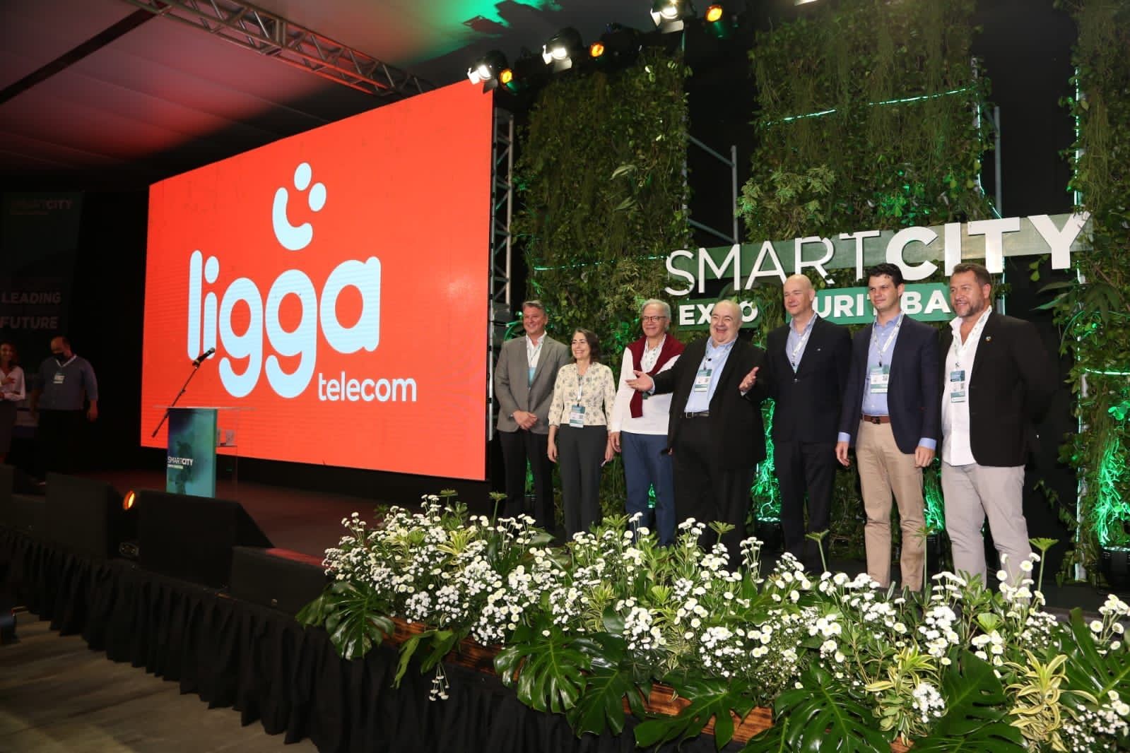 Fila com nomes da empresa, com logo em laranja escrito Ligga Telecom ao fundo