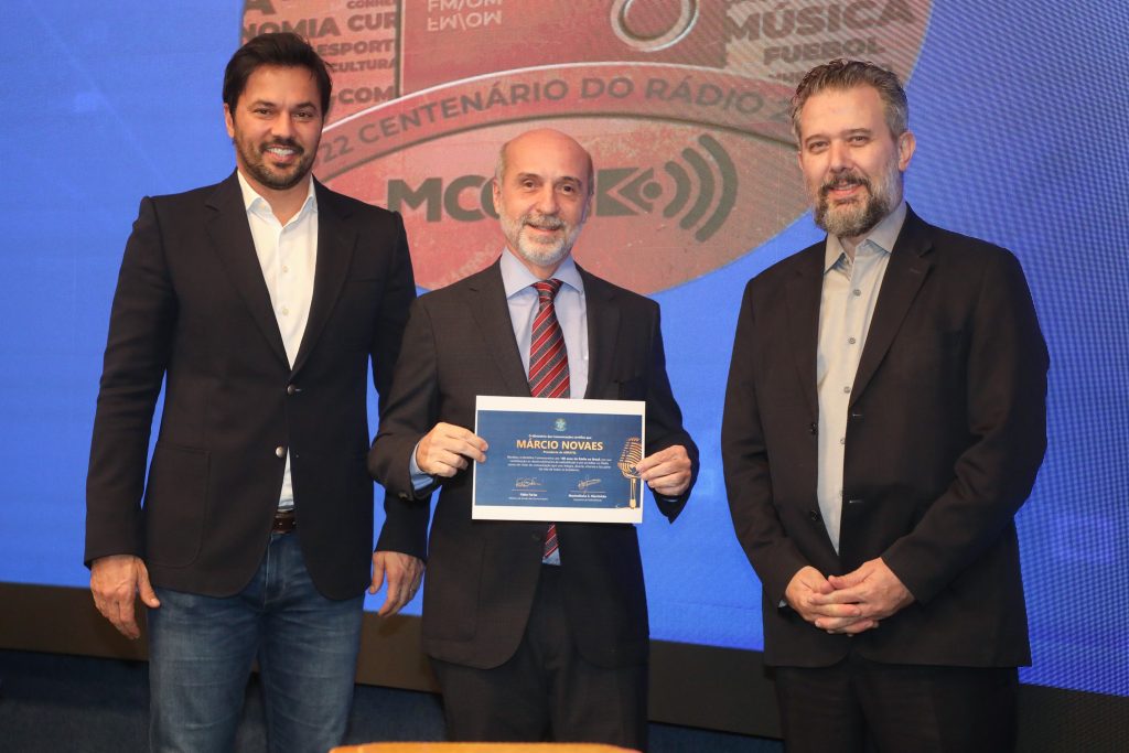 O presidente da Abratel, Márcio Novaes (ao centro), recebendo o selo especial em comemoração ao centenário do rádio. Ao seu lado, o ministro das comunicações. Fábio Faria.